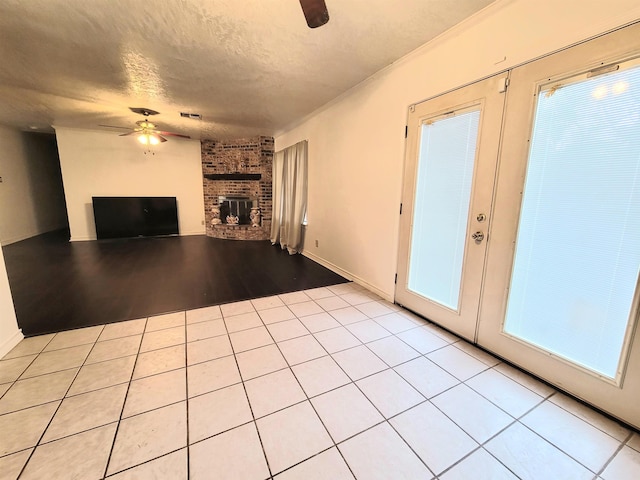 unfurnished living room with a textured ceiling, visible vents, a ceiling fan, a brick fireplace, and light tile patterned floors