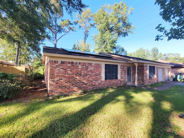 view of front of house featuring an attached garage, brick siding, solar panels, and a front lawn
