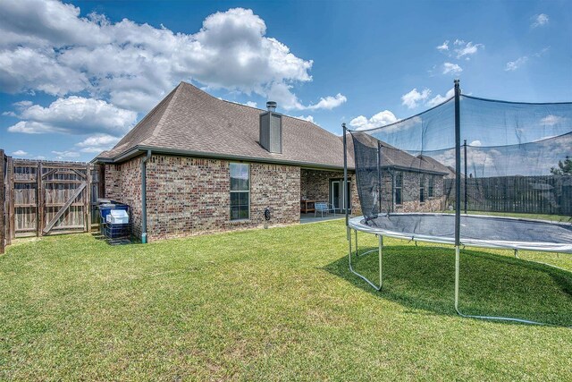 232 Spring Brook Ct, Lumberton, TX 77657 - back of property featuring a trampoline, brick siding, a gate, a chimney, and roof with shingles