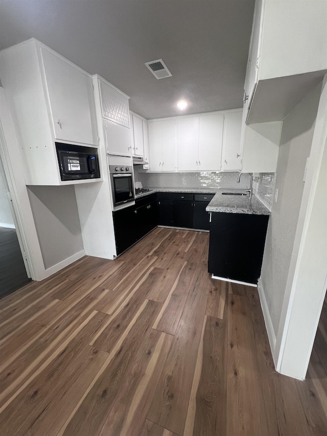 kitchen featuring stainless steel oven, sink, dark hardwood / wood-style floors, decorative backsplash, and white cabinetry