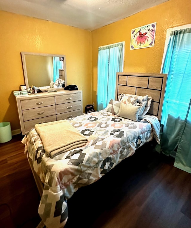 bedroom with multiple windows, dark wood-style floors, baseboards, and a textured wall