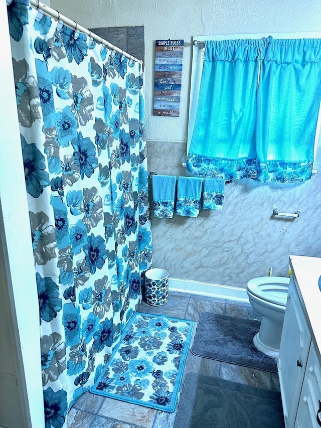 full bath with vanity, stone tile floors, toilet, and a shower with curtain