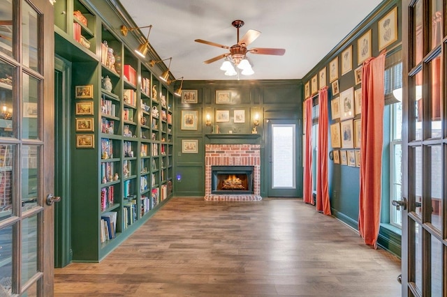 unfurnished room featuring hardwood / wood-style flooring, ceiling fan, built in features, a fireplace, and ornamental molding