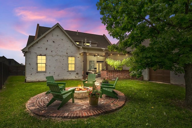 back house at dusk with ceiling fan, a yard, and a fire pit