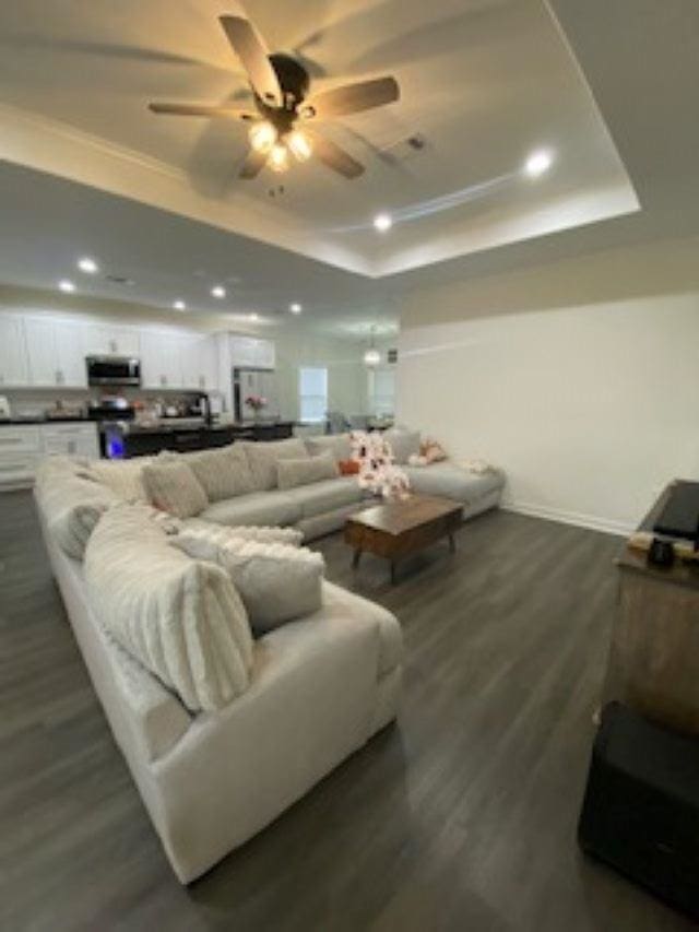 living room featuring dark hardwood / wood-style flooring, a raised ceiling, ceiling fan, and ornamental molding