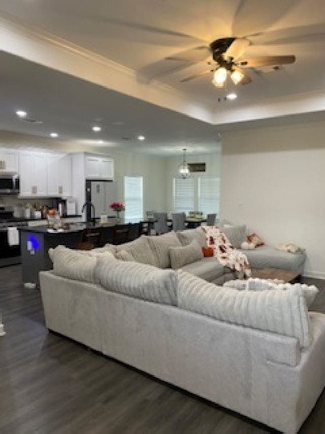 living room with dark hardwood / wood-style floors, ceiling fan, a raised ceiling, and crown molding