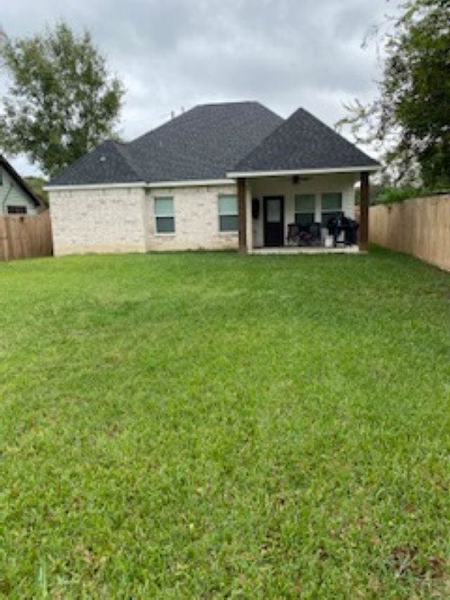 rear view of house featuring ceiling fan and a yard