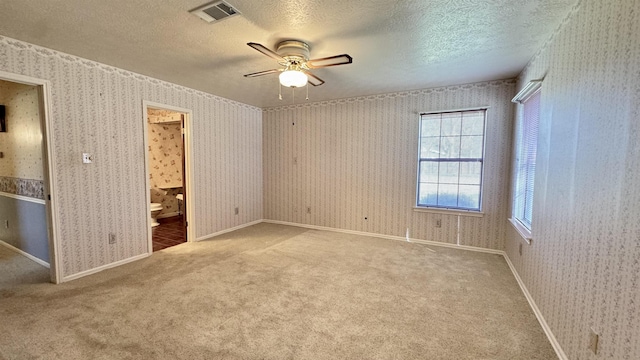 unfurnished bedroom with ensuite bath, a textured ceiling, ceiling fan, and carpet