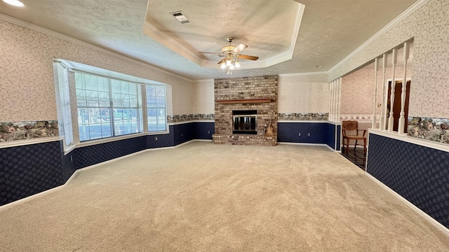 living room featuring a raised ceiling, crown molding, carpet, a fireplace, and ceiling fan