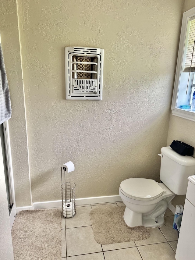 bathroom with baseboards, toilet, tile patterned flooring, and a textured wall