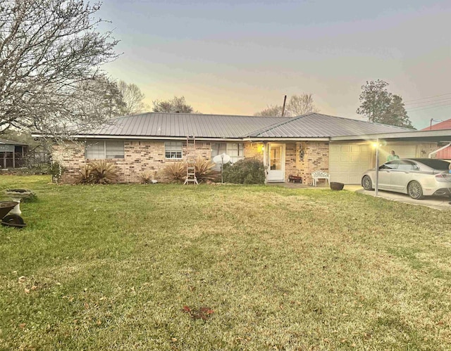 ranch-style home featuring metal roof, brick siding, a lawn, and an attached garage