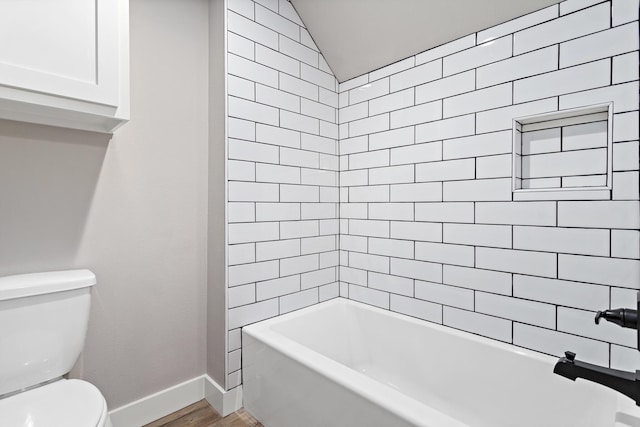 bathroom with vaulted ceiling, wood-type flooring, tiled shower / bath combo, and toilet