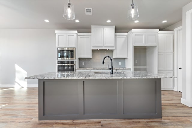 kitchen featuring decorative light fixtures, white cabinetry, and an island with sink