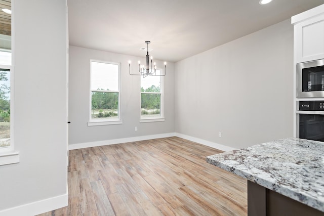 unfurnished dining area with light hardwood / wood-style floors and an inviting chandelier