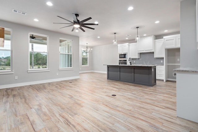 kitchen with backsplash, a kitchen island with sink, decorative light fixtures, an inviting chandelier, and white cabinetry