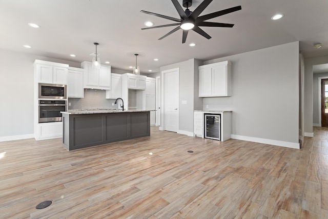 kitchen featuring stainless steel oven, built in microwave, a center island with sink, white cabinetry, and hanging light fixtures