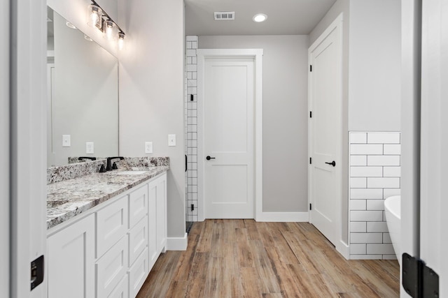 bathroom with vanity, wood-type flooring, a bath, and tile walls