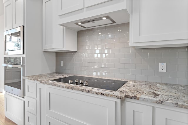 kitchen with white cabinets, black electric stovetop, backsplash, and light stone counters