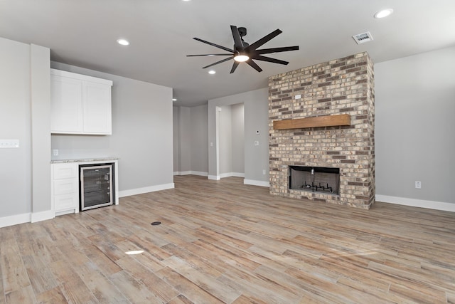 unfurnished living room featuring wine cooler, ceiling fan, a fireplace, and light hardwood / wood-style floors