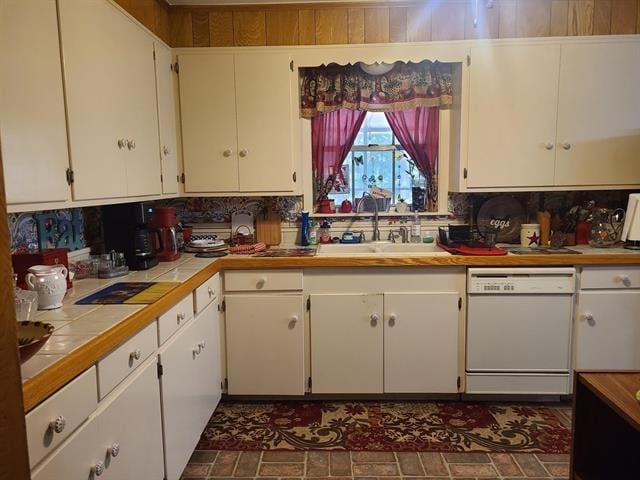 kitchen with tile counters, dishwasher, white cabinets, and sink