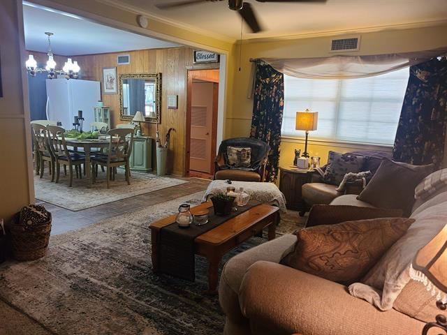 living room featuring ceiling fan with notable chandelier, wood walls, and ornamental molding