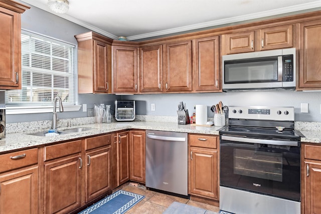 kitchen with light stone countertops, appliances with stainless steel finishes, brown cabinetry, and a sink