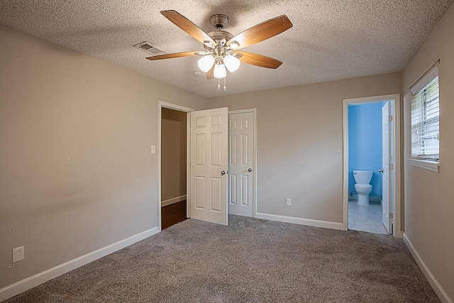 unfurnished bedroom featuring ensuite bath, ceiling fan, a textured ceiling, and dark colored carpet