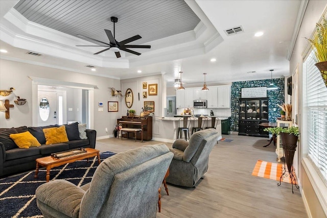 living room with a tray ceiling, ceiling fan, plenty of natural light, and ornamental molding