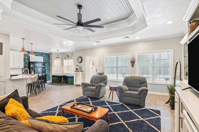 living room featuring a tray ceiling, ceiling fan, light hardwood / wood-style floors, and ornamental molding