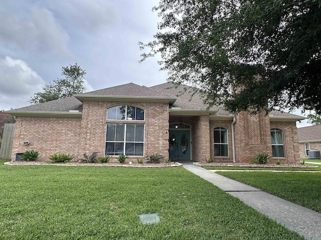 view of front of property with a shingled roof, cooling unit, brick siding, and a front yard