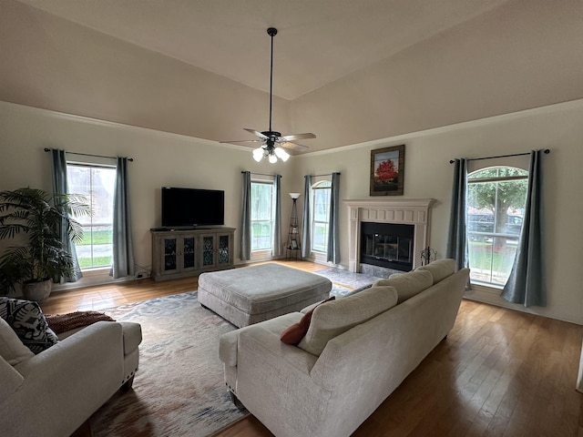 living area featuring a glass covered fireplace, wood finished floors, lofted ceiling, and ceiling fan