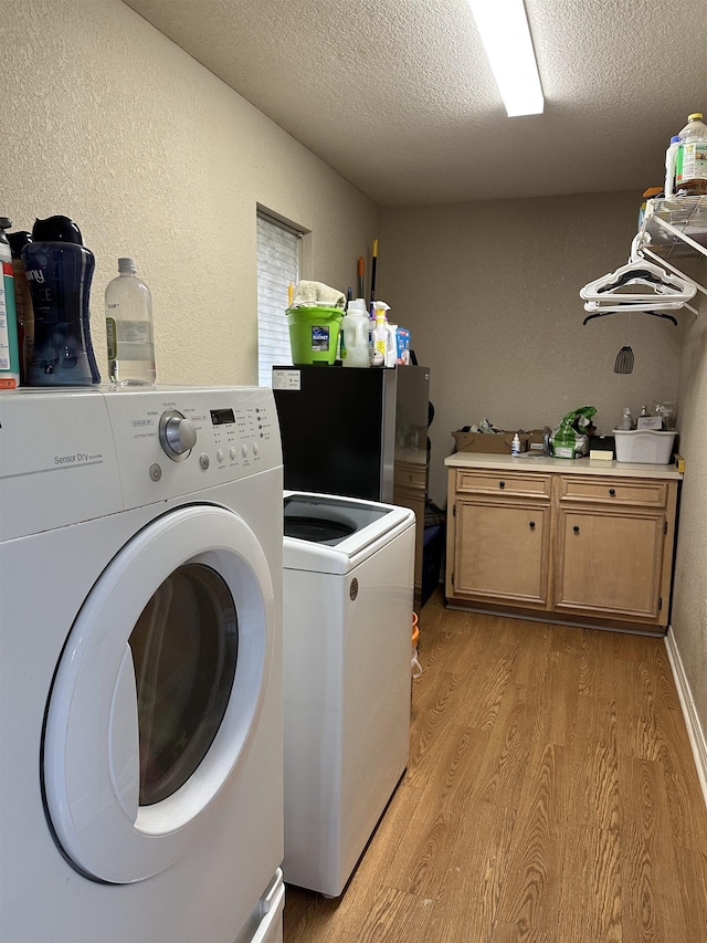 washroom featuring a textured wall, washer and dryer, light wood-type flooring, a textured ceiling, and cabinet space