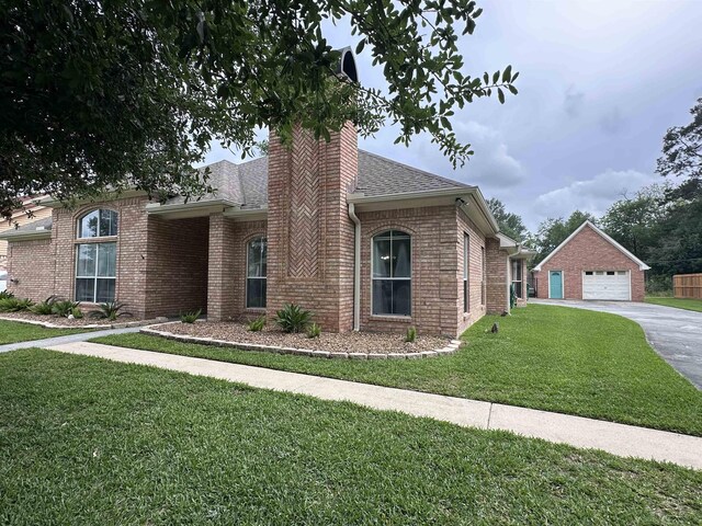 ranch-style home with roof with shingles, an outbuilding, a garage, brick siding, and a front lawn