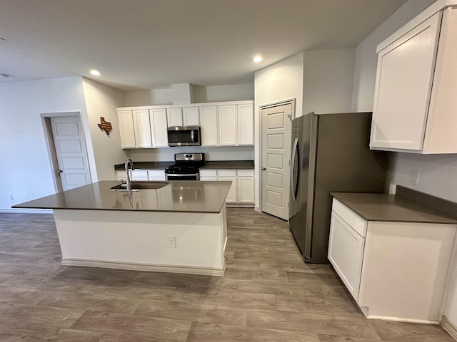 kitchen featuring sink, light wood-type flooring, appliances with stainless steel finishes, a kitchen island with sink, and white cabinets