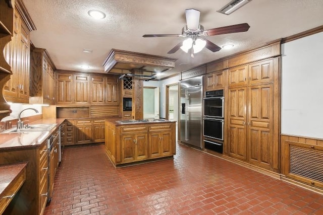 kitchen with sink, stainless steel appliances, a center island, ornamental molding, and a textured ceiling