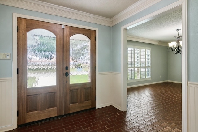 foyer featuring crown molding, a textured ceiling, french doors, and a chandelier