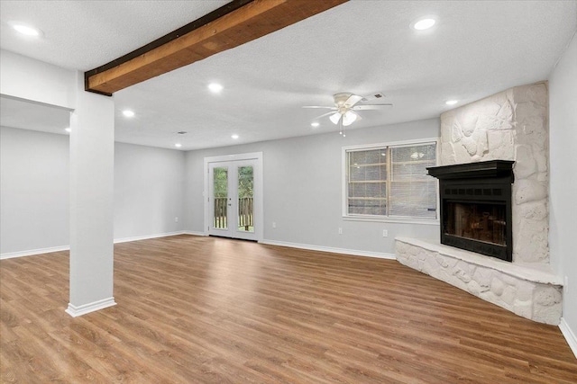 unfurnished living room with beam ceiling, ceiling fan, hardwood / wood-style floors, a textured ceiling, and a fireplace