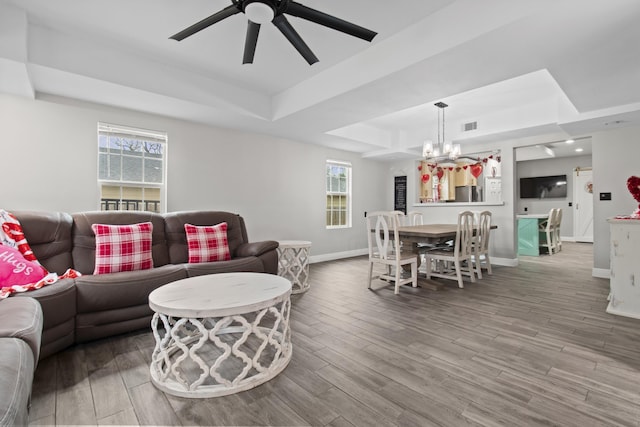 living room featuring ceiling fan with notable chandelier, wood-type flooring, and a tray ceiling