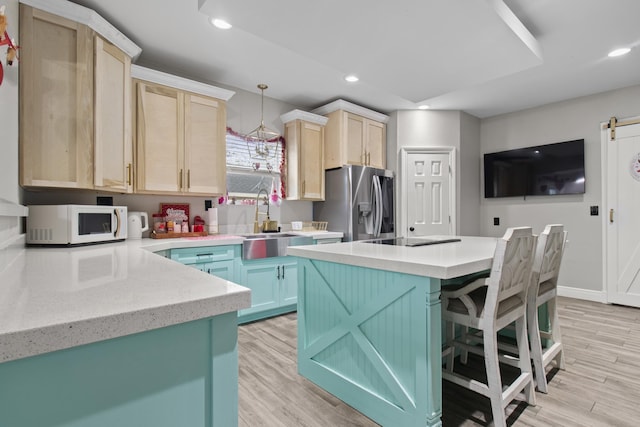 kitchen with a barn door, stainless steel refrigerator with ice dispenser, decorative light fixtures, light brown cabinetry, and a kitchen island