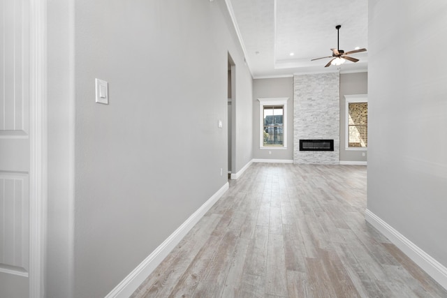 unfurnished living room featuring ceiling fan, a raised ceiling, a stone fireplace, light hardwood / wood-style flooring, and ornamental molding