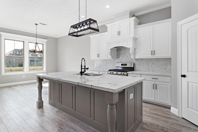 kitchen with light stone countertops, gas range, white cabinetry, and sink