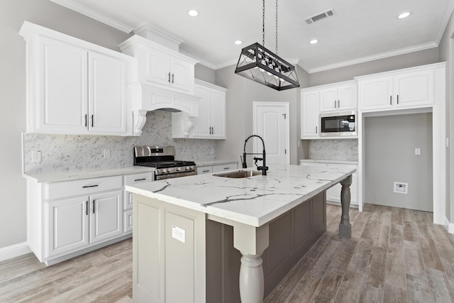 kitchen with white cabinetry, sink, stainless steel appliances, light stone counters, and a center island with sink