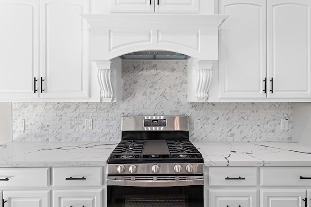 kitchen featuring custom exhaust hood, stainless steel gas range oven, decorative backsplash, light stone countertops, and white cabinetry