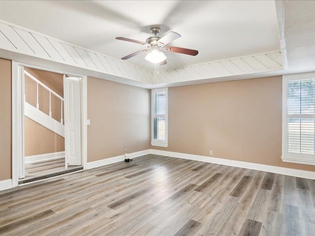 empty room featuring hardwood / wood-style floors, a raised ceiling, a wealth of natural light, and ceiling fan