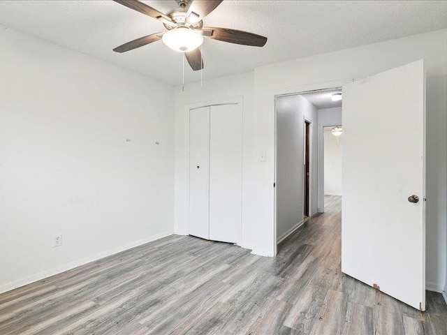 unfurnished bedroom featuring a textured ceiling, wood-type flooring, a closet, and ceiling fan