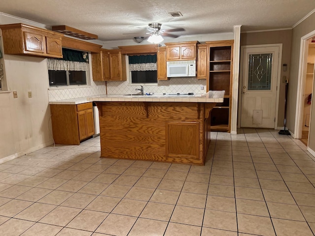 kitchen with light tile patterned flooring, ceiling fan, ornamental molding, a textured ceiling, and a kitchen island