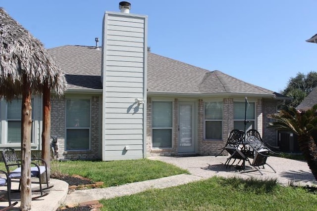 rear view of property featuring a yard, a patio, a chimney, and roof with shingles