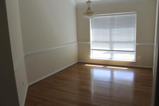 spare room with baseboards, wood finished floors, an inviting chandelier, and ornamental molding