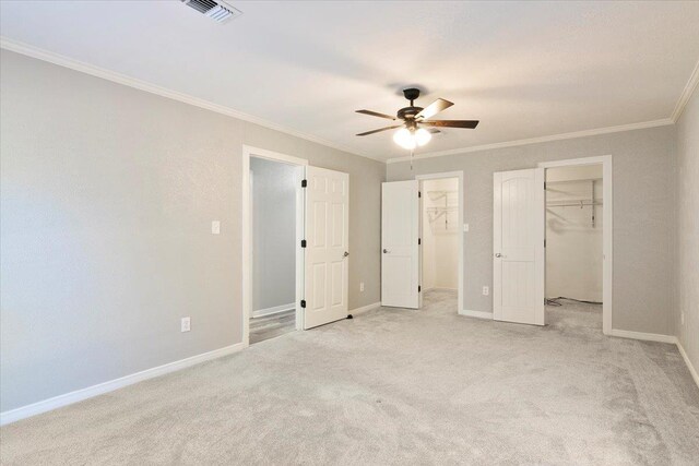 unfurnished bedroom featuring light carpet, a spacious closet, ceiling fan, and crown molding