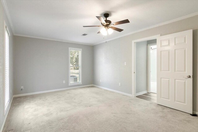 carpeted empty room featuring ceiling fan, crown molding, and a wealth of natural light